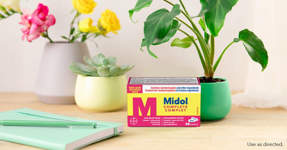 Box of Midol on a desk between two flowers